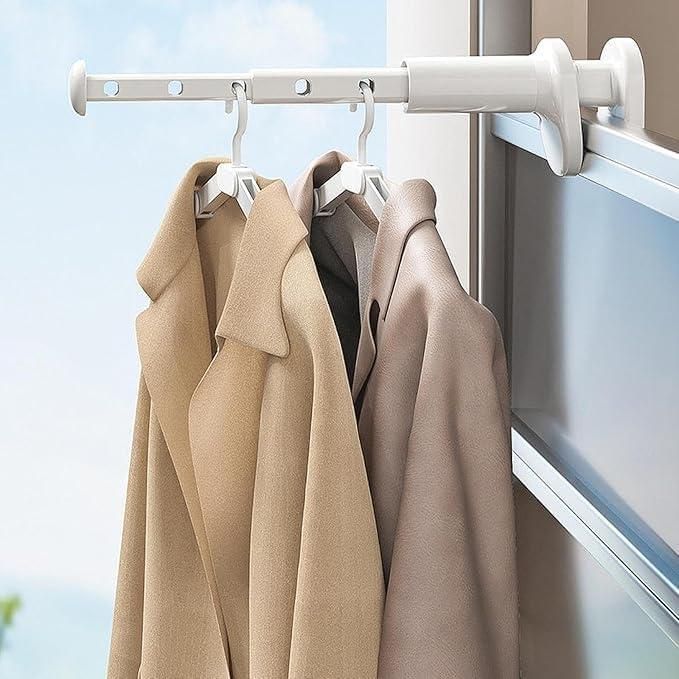 Three beige coats hanging on a white rod against a window with blue sky.