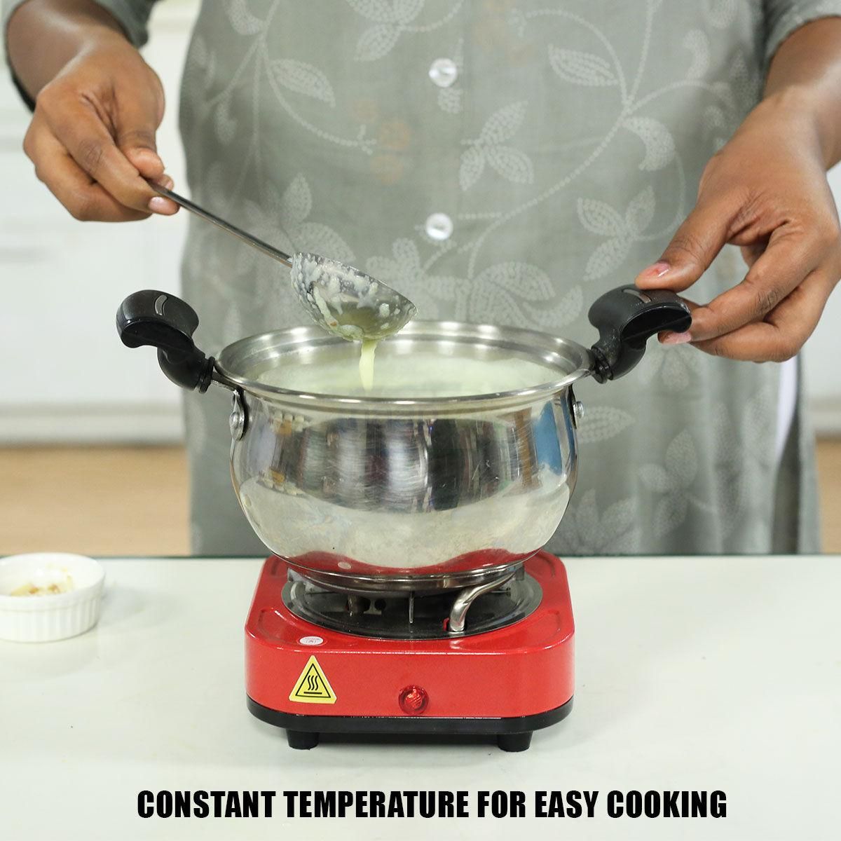 Person using a red hot plate with a metal pot and strainer, stirring contents.