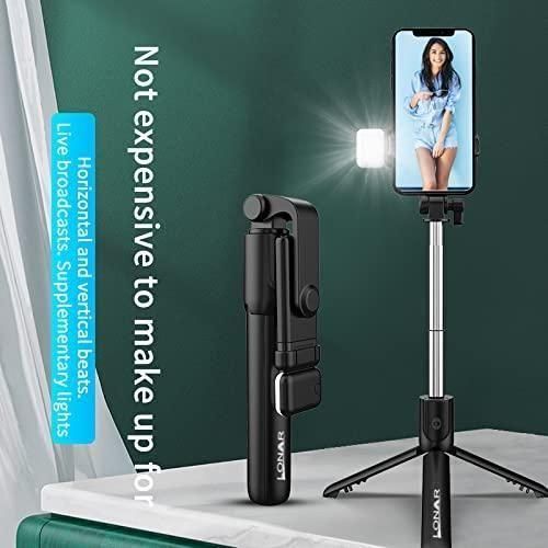 Black selfie stick with smartphone holder and light on a white surface with green background
